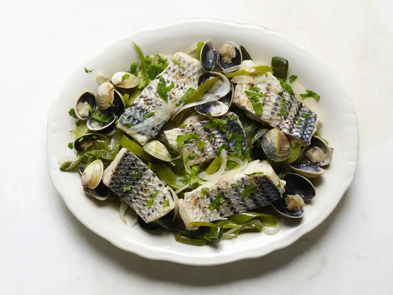 A delicious bonito fish recipe with clams, onions, and herbs, served on a white platter.