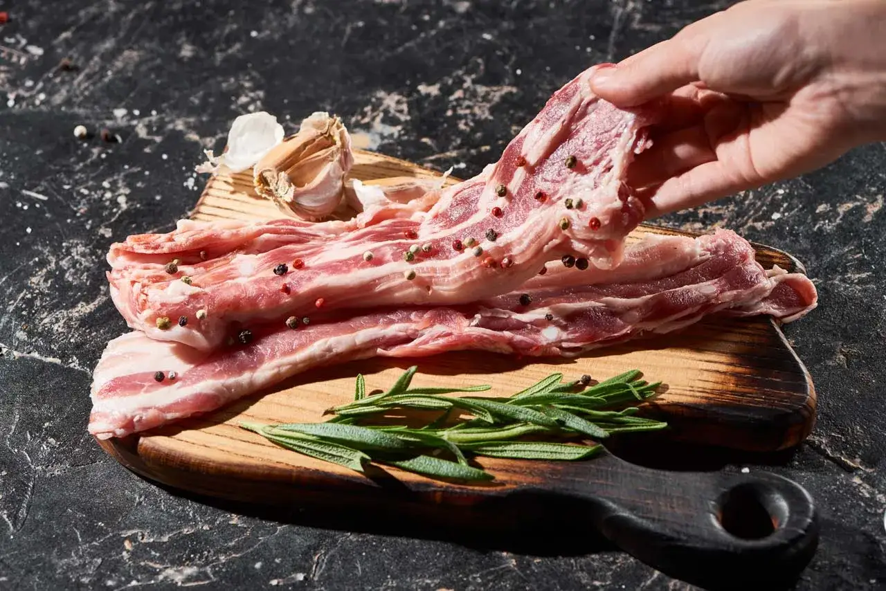Raw Iberico pork belly strips seasoned with peppercorns and garlic, ready for cooking. Learn how to cook Iberico pork for a delicious meal.