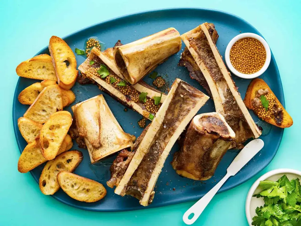 Roasted bone marrow halves served with toasted baguette slices, whole grain mustard, and parsley. A delicious bone marrow recipe.