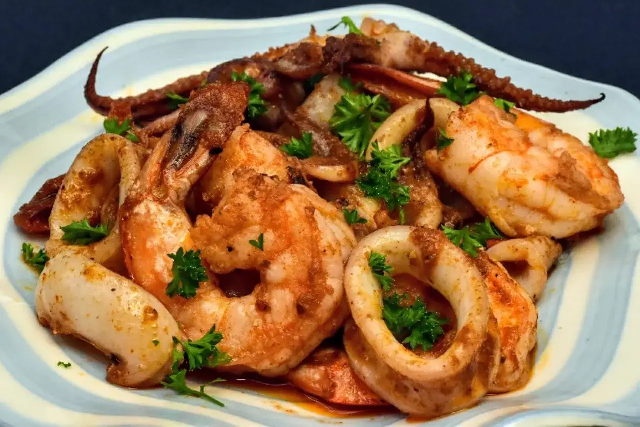 A delicious Spanish seafood dish featuring grilled squid rings, shrimp, and octopus tentacles, garnished with fresh parsley.