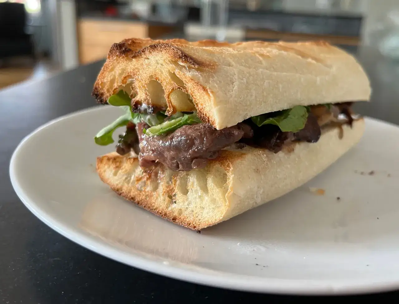 A delicious pepito sandwich with tender meat and fresh greens on a toasted baguette, ready to be devoured.