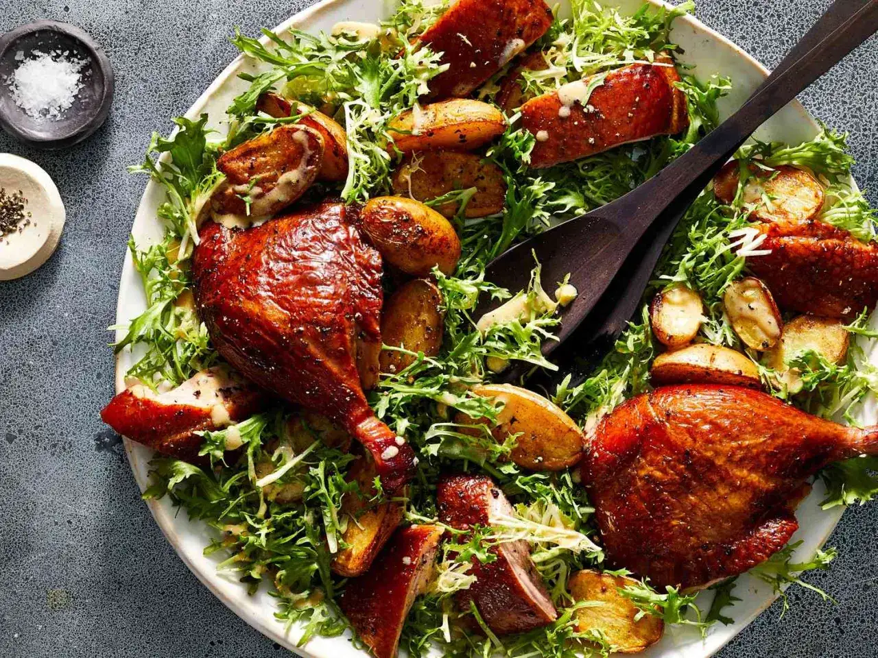 A hearty salad featuring tender, glazed smoked duck legs, crispy roasted potatoes, and fresh greens, all drizzled with a creamy dressing.