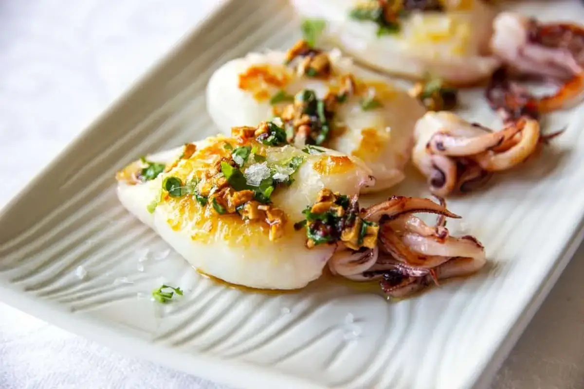 Tender baby squid food, grilled and topped with herbs and garlic, served on a white platter.