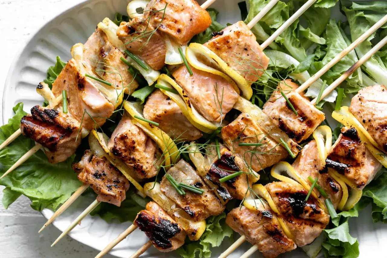 Grilled salmon skewers with lemon slices and chives, served on a bed of crisp lettuce.