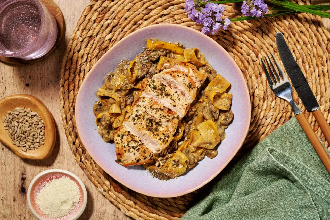 A delicious plate of chicken tapas featuring sliced grilled chicken breast over creamy pasta with mushrooms and herbs.