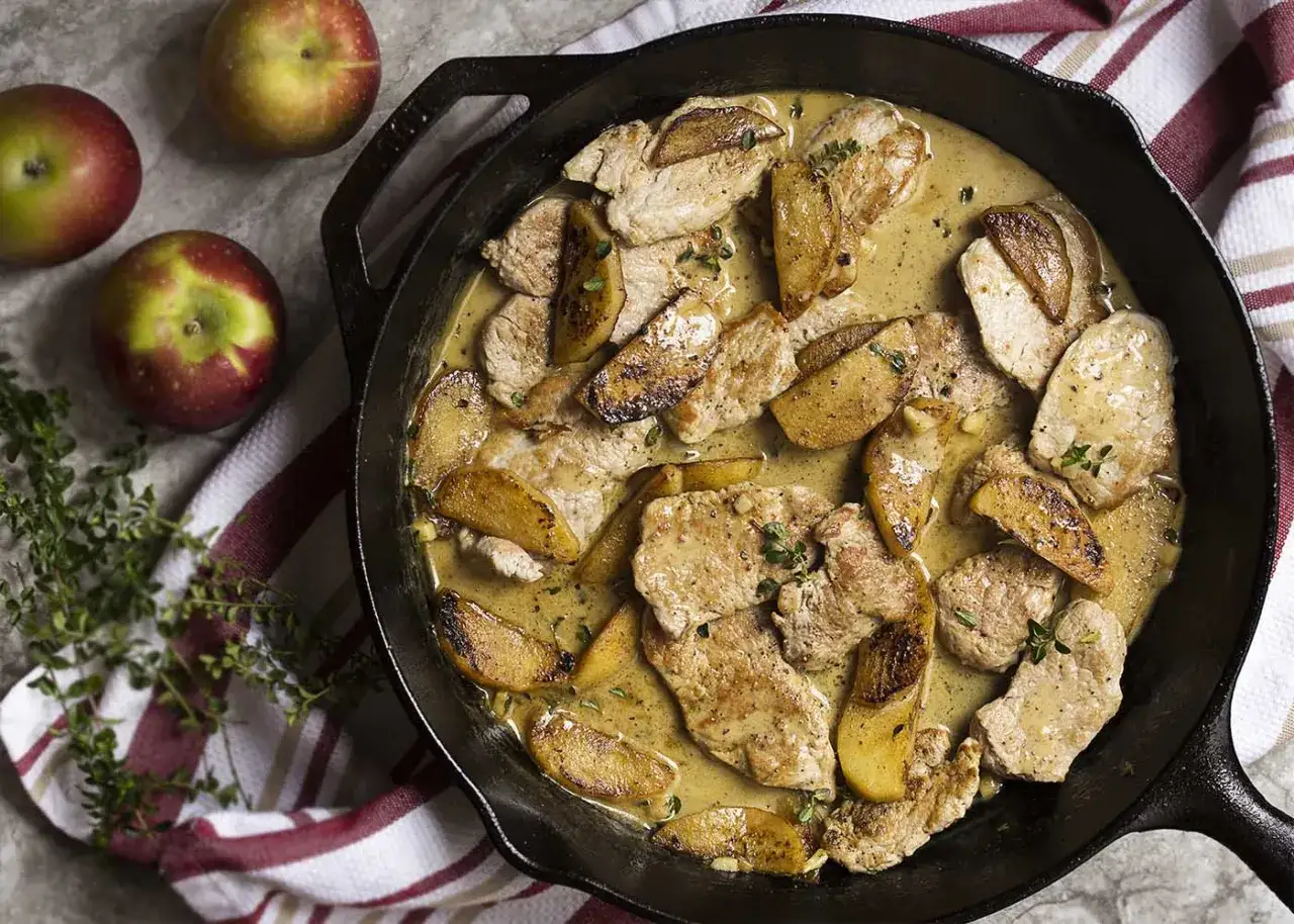 Pork tenderloin slices with caramelized apples in a creamy sauce, a delicious solomillo recipe, garnished with fresh thyme.