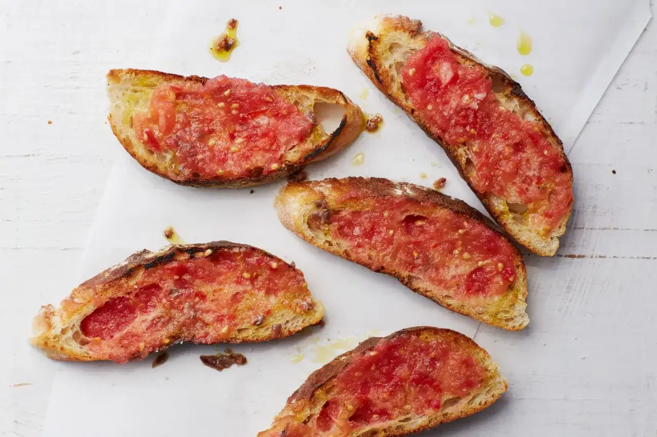 Five slices of toasted bread topped with grated tomato and olive oil, a classic pan con tomate.
