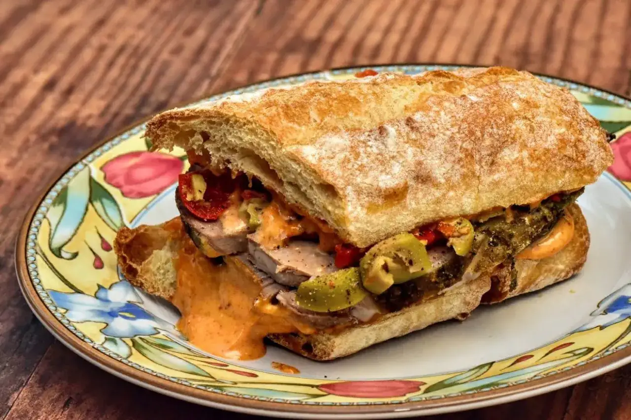 A delicious lamb bocadillo overflowing with tender meat, olives, and a creamy sauce, served on a rustic bun.