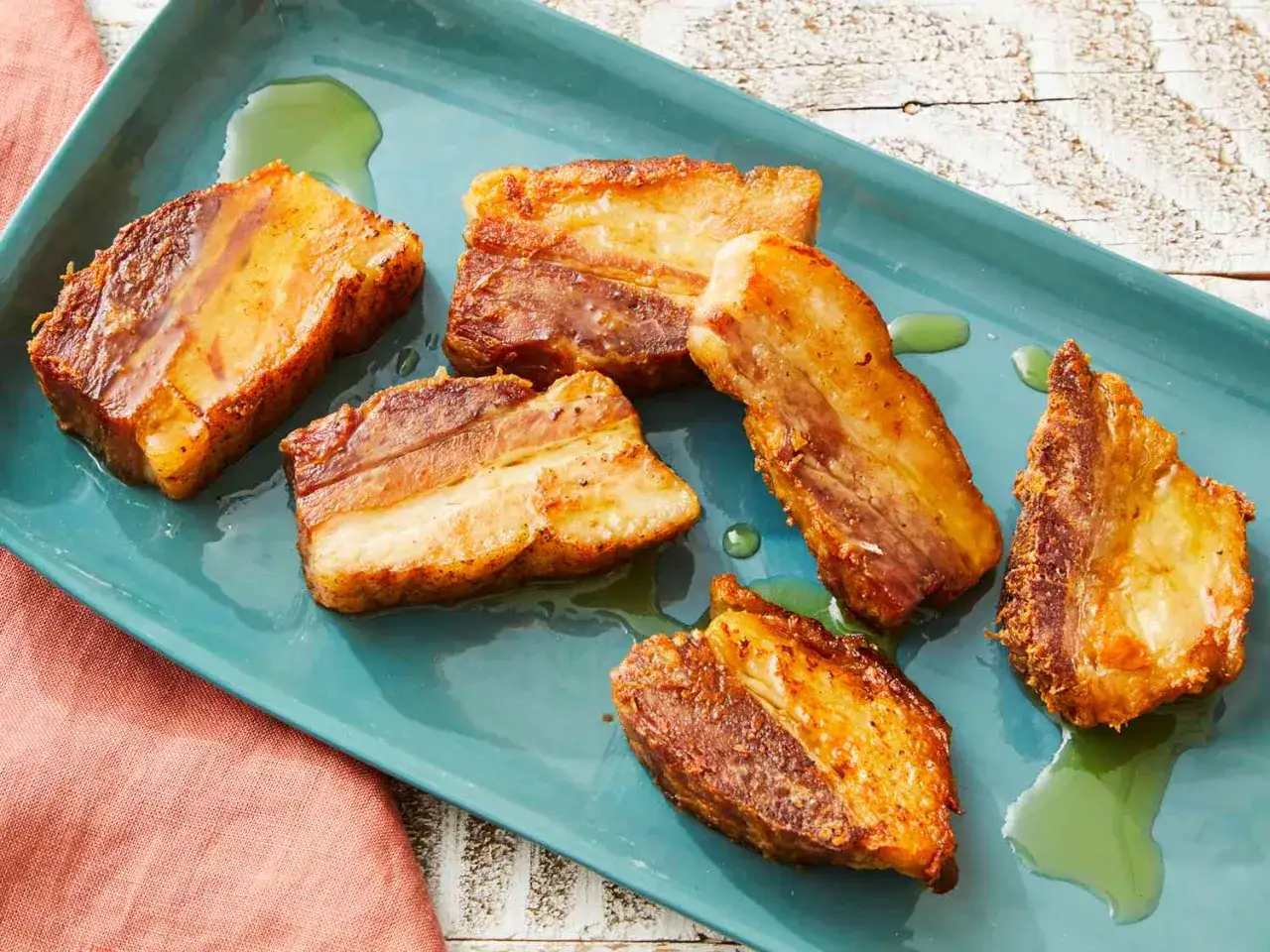 Crispy pork belly, Spanish style, glistening on a teal platter with a hint of green oil.