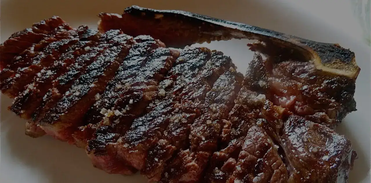 A perfectly grilled Spanish steak, sliced and seasoned with coarse salt, showcases its juicy, pink interior and charred crust.