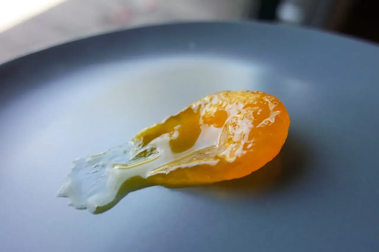 A bright orange, glistening salt cured egg yolk sits on a dark grey plate, its edges melting slightly.