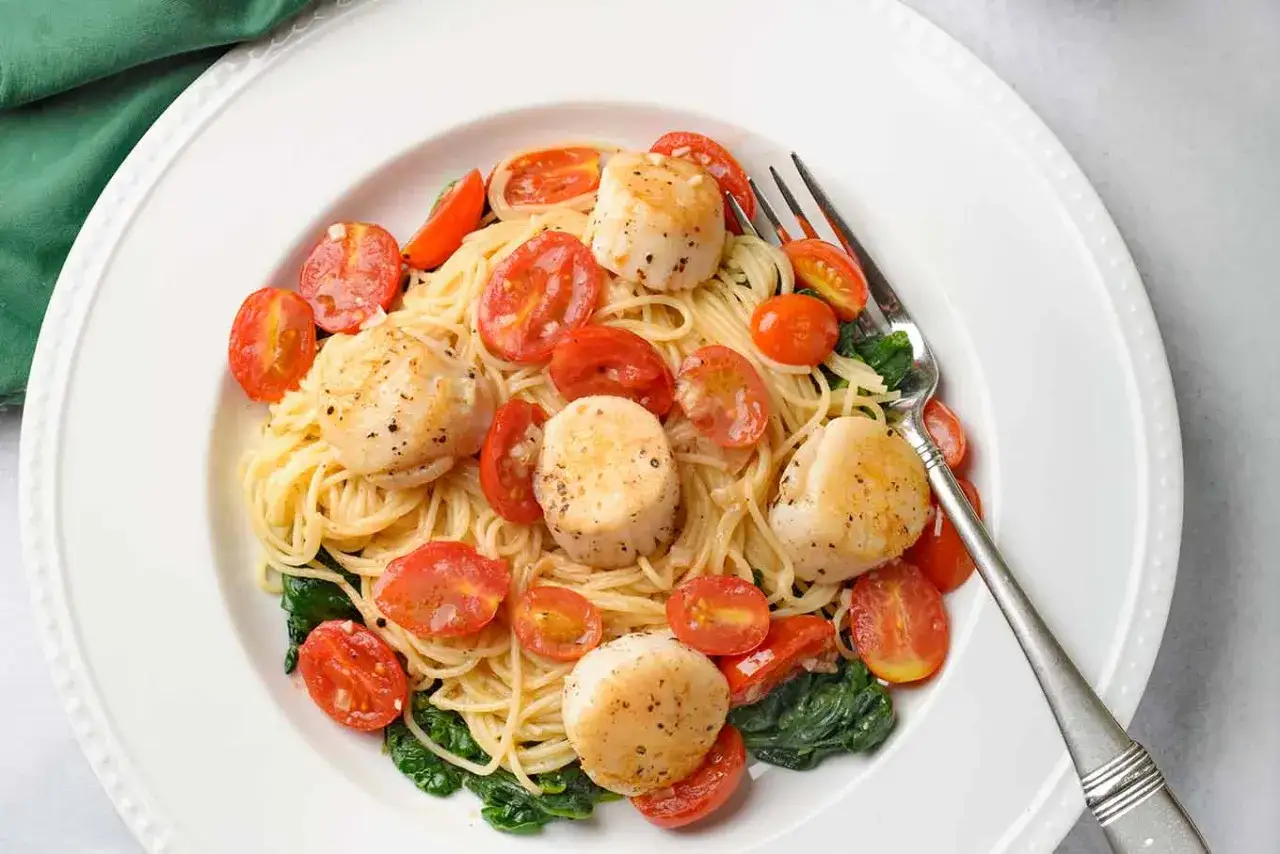 Scallops and pasta recipe with cherry tomatoes and spinach, finished with a white wine sauce.