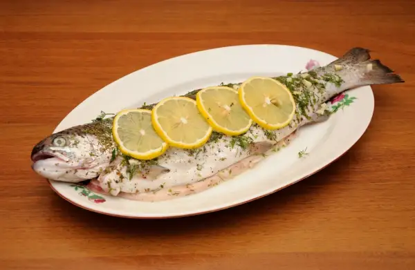 A whole trout, seasoned and garnished with lemon slices and herbs, ready to be cooked as trucha a la navarra.