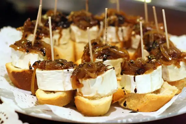 Delicious pincho recipes: bite-sized bread topped with creamy cheese, caramelized onions, and a balsamic glaze, all secured with a toothpick.