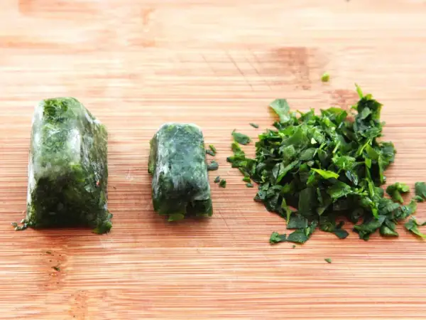 Learn how to freeze fresh herbs: two frozen herb blocks and a pile of chopped herbs on a wooden cutting board.