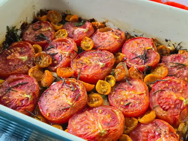A baking dish filled with juicy, slow roasted tomatoes and cherry tomatoes, seasoned with herbs and spices.