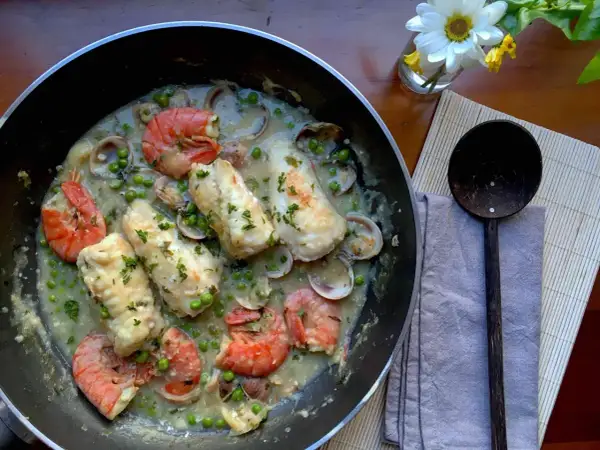 A delicious bonito fish recipe with prawns, clams, and peas in a creamy sauce, garnished with parsley.