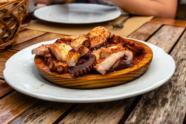 A delicious Spanish octopus dish, seasoned with paprika and served on a wooden platter on a rustic table.