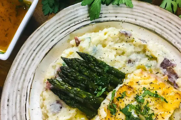 A delicious grouper recipe featuring pan-seared fish, creamy mashed potatoes with red skin, and roasted asparagus, all garnished with fresh parsley.