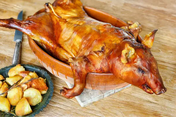 A whole roasted suckling pig, golden brown and glistening, sits in a rustic clay dish. This image evokes delicious suckling pig recipes and a feast.