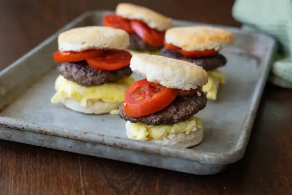 Fluffy biscuits layered with scrambled eggs, a savory goose sausage patty, and fresh tomato slices.