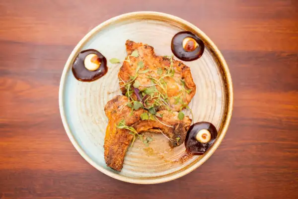 Two pieces of grilled steak, garnished with microgreens, are served as steak tapas with a rich sauce and a dollop of cream.