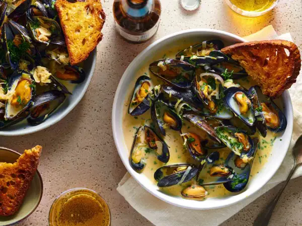 A delicious bowl of moules marinière, brimming with plump mussels in a creamy broth, served with crusty bread and a glass of beer.
