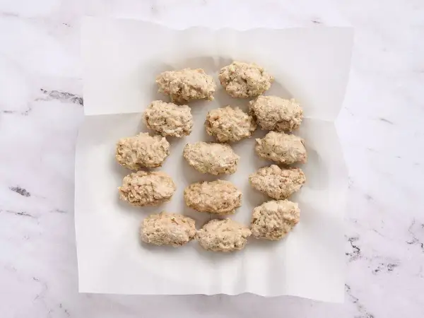 A dozen uncooked croquetas de pollo are arranged on white parchment paper, ready for frying.