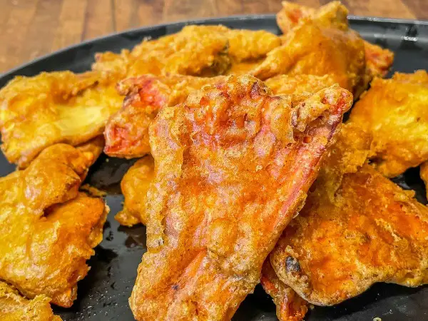 Crispy, golden-fried pieces, possibly part of a delicious chicken of the woods recipe, piled on a black plate.