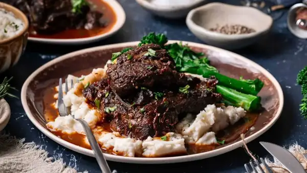 Tender beef cheek, Spanish style, served with creamy mashed potatoes and vibrant green vegetables.