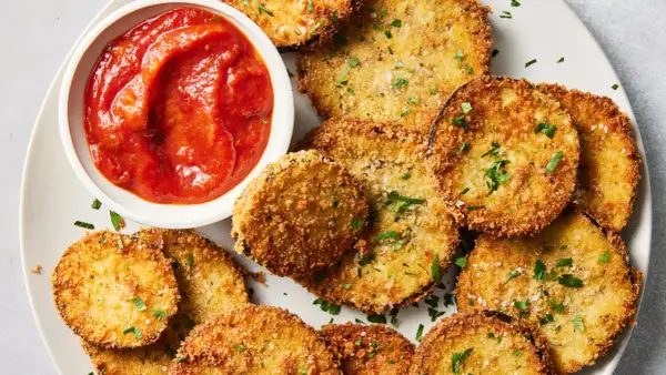 Crispy spanish fried eggplant slices, golden brown and seasoned, served with a side of vibrant tomato sauce and sprinkled with fresh parsley.