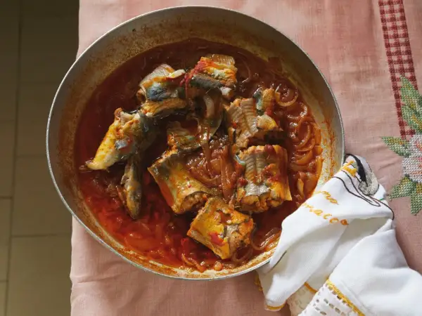 A rustic pan of eel recipes, featuring chunks of eel simmered in a rich, tomato-based sauce with onions.