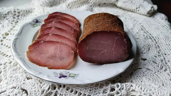 A whole and sliced cured pork loin, seasoned with spices, rests on a decorative plate.