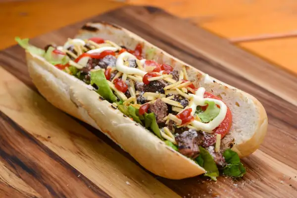 A delicious pepito sandwich overflowing with tender steak, crisp lettuce, tomato, shoestring fries, and drizzled with ketchup and mayonnaise.