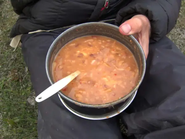 A hearty bowl of gulas fish stew, served in a metal pot with a white spoon, ready for a meal outdoors.