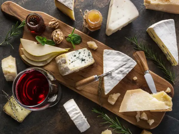 A beautiful spread of wine and cheese pairings, featuring a glass of red wine, various cheeses, pears, walnuts, and honey on a wooden board.