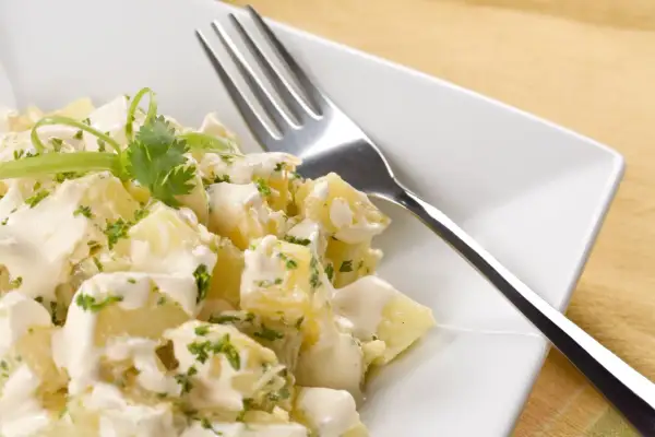 A delicious ensalada rusa española, featuring creamy potato salad with fresh herbs and a fork ready to dig in.