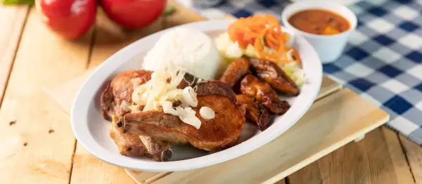 A delicious plate of chuleta meat, a flavorful pork chop, served with rice, fried plantains, salad, and beans.