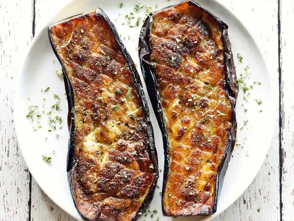 Two halves of baked eggplant, seasoned and sprinkled with herbs, are a delicious start to many eggplant recipes.