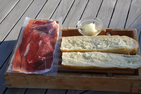 Ingredients for a delicious jamon iberico sandwich: thinly sliced cured ham, buttered bread rolls, and a small dish of butter.