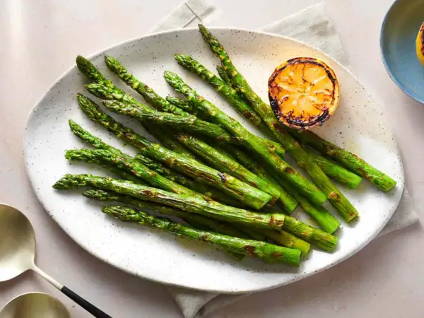 A plate of perfectly grilled spanish asparagus, lightly charred and served with a grilled lemon slice.