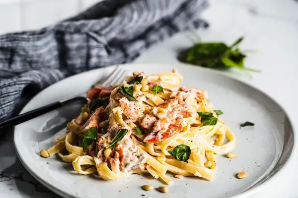 A plate of creamy smoked salmon pasta, garnished with fresh basil and pine nuts.