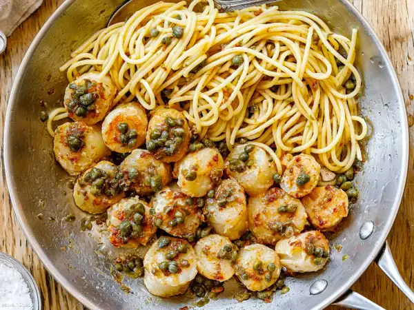 A delicious scallops and pasta recipe with white wine sauce, garnished with capers, served in a skillet.