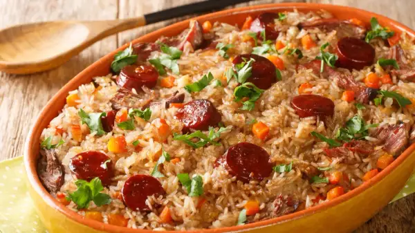 A hearty dish of rice with sauteed chorizo, tender meat, and diced carrots, garnished with fresh parsley.