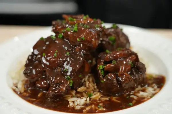 Tender, braised oxtail pieces in a rich, dark sauce, served over fluffy white rice and garnished with chopped green onions. A delicious oxtail recipe.