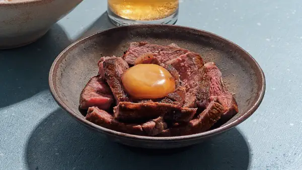 Sliced steak in a bowl topped with a glistening salt cured egg yolk, ready to be mixed into a rich, savory dish.