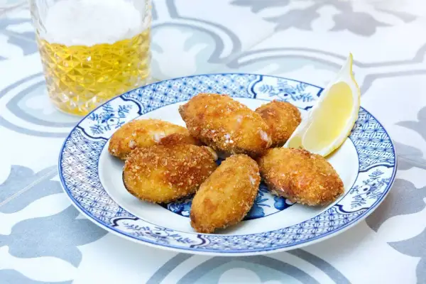 Crispy fried tiger mussels served on a blue and white plate with a lemon wedge and a glass of beer.