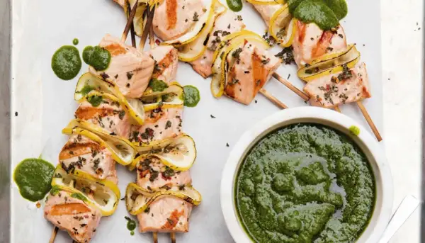 Grilled salmon skewers with lemon slices and a vibrant green sauce, ready to be dipped.