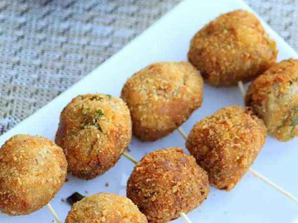 Golden-brown tuna balls on skewers, coated in crispy breadcrumbs, are arranged on a white platter.